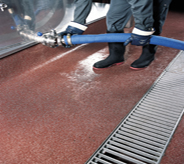 Worker with hose drains cement atop red floor coating.